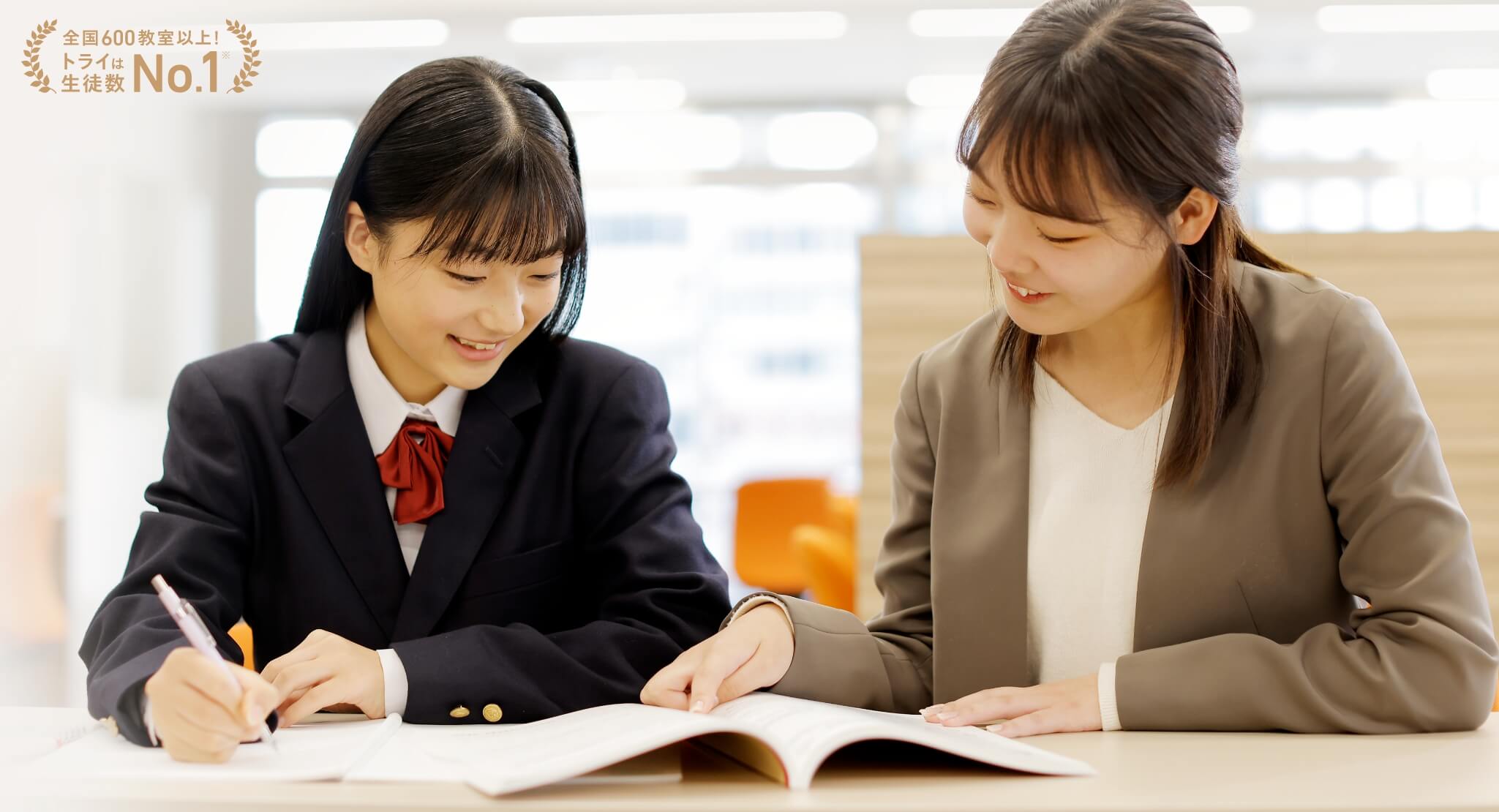 教科書を見ながら優しく教える女性の先生と安心して話を聞いている女性の生徒